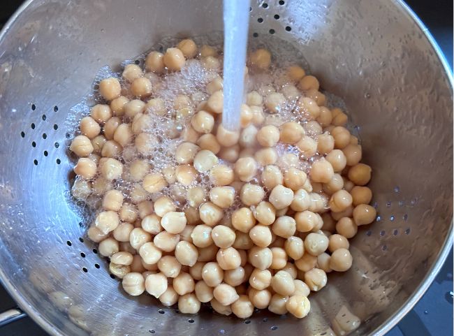 Kichererbsen sind in einem Sieb und Wasser l&auml;uft dar&uuml;ber